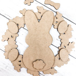 May include: A wooden craft kit for making an Easter bunny wreath. The kit includes a bunny cutout, a bow, eggs, and flowers.