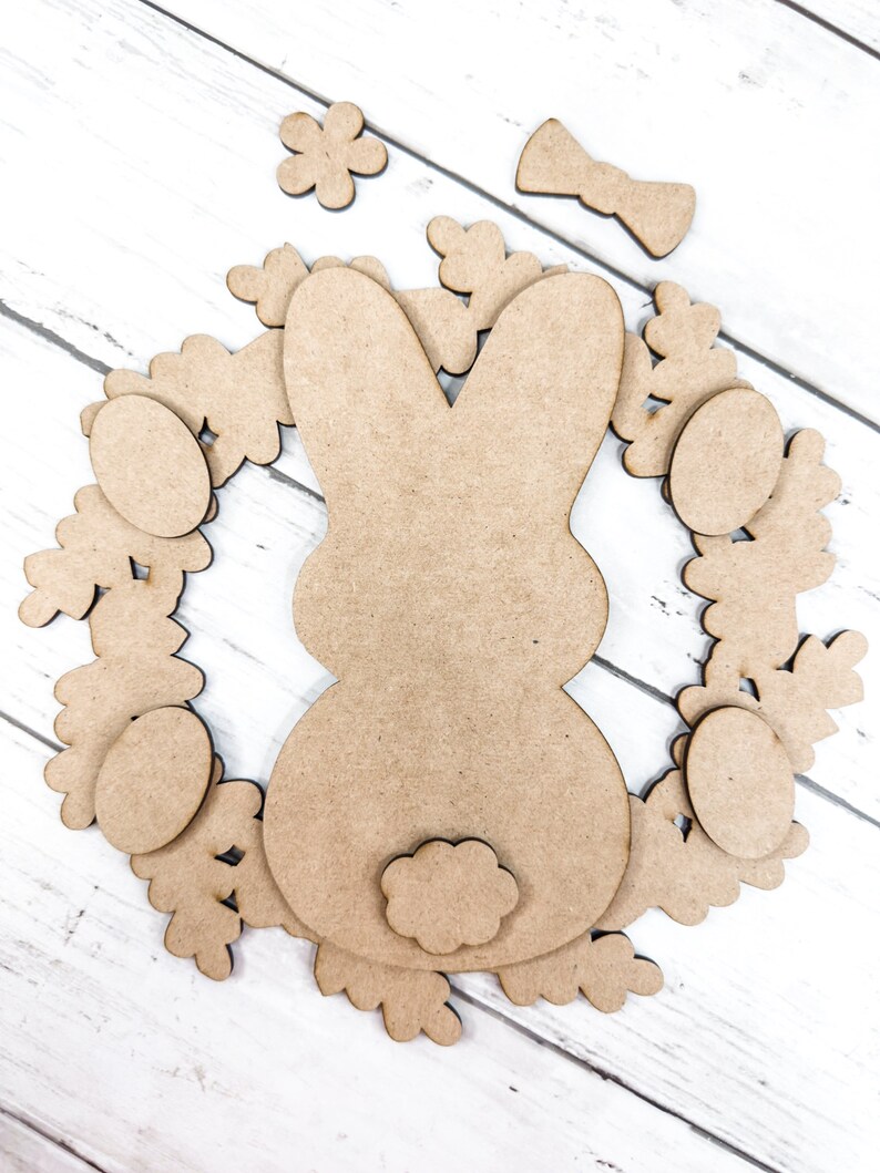 May include: A wooden craft kit for making an Easter bunny wreath. The kit includes a bunny cutout, a bow, eggs, and flowers.