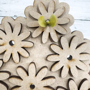May include: A wooden craft project featuring a design of multiple overlapping flowers. The flowers are cut out of wood and have a brown color. A small yellow flower is placed in the center of the design.