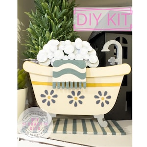 May include: DIY craft kit featuring a white bathtub with a blue and white striped towel, white foam bubbles, and a yellow rim. The bathtub has three blue flowers on the front. The kit includes the text "DIY KIT" in pink.