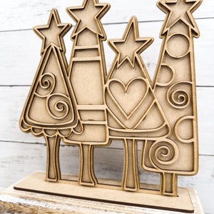 Op de afbeelding: Houten kerstboomuitsparing met een ster bovenop. De boom is versierd met spiralen en cirkels. De uitsparing staat op een houten basis.