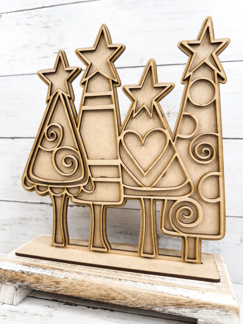 Op de afbeelding: Houten kerstboomuitsparing met een ster bovenop. De boom is versierd met spiralen en cirkels. De uitsparing staat op een houten basis.