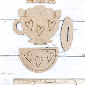 Op de afbeelding: Houten knutselset met een theekopje met hartjes, een deksel en een aparte schotel. De set is bedoeld om in elkaar te zetten en te beschilderen.