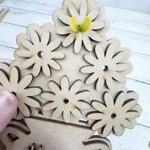 May include: A wooden craft project featuring a vase with a bouquet of flowers. The vase is decorated with the words "Happy Mother's Day". A yellow butterfly is perched on top of the flowers.