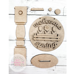 May include: Wooden craft kit for a welcome spring sign. The kit includes a round sign with the words "welcome spring" and a flower design, a post, a birdhouse, and a small oval piece.