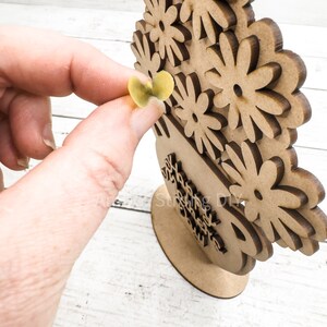 May include: Wooden craft project featuring a vase with flowers. The vase has the words "Happy Mother's Day" written on it. The flowers are made of individual pieces of wood that can be painted or decorated.