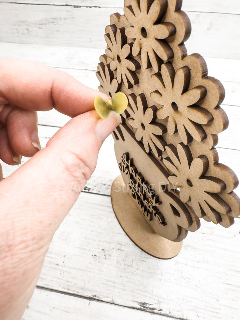 May include: Wooden craft project featuring a vase with flowers. The vase has the words "Happy Mother's Day" written on it. The flowers are made of individual pieces of wood that can be painted or decorated.