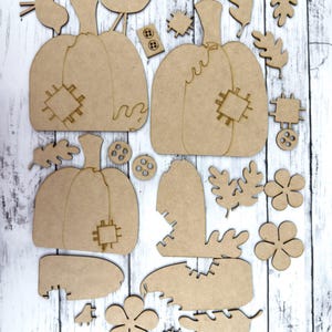 May include: A set of unfinished wooden pumpkin and leaf shapes for crafting. The set includes two large pumpkins, two small pumpkins, a bird, leaves, and flowers. The pumpkins have a stitched design.
