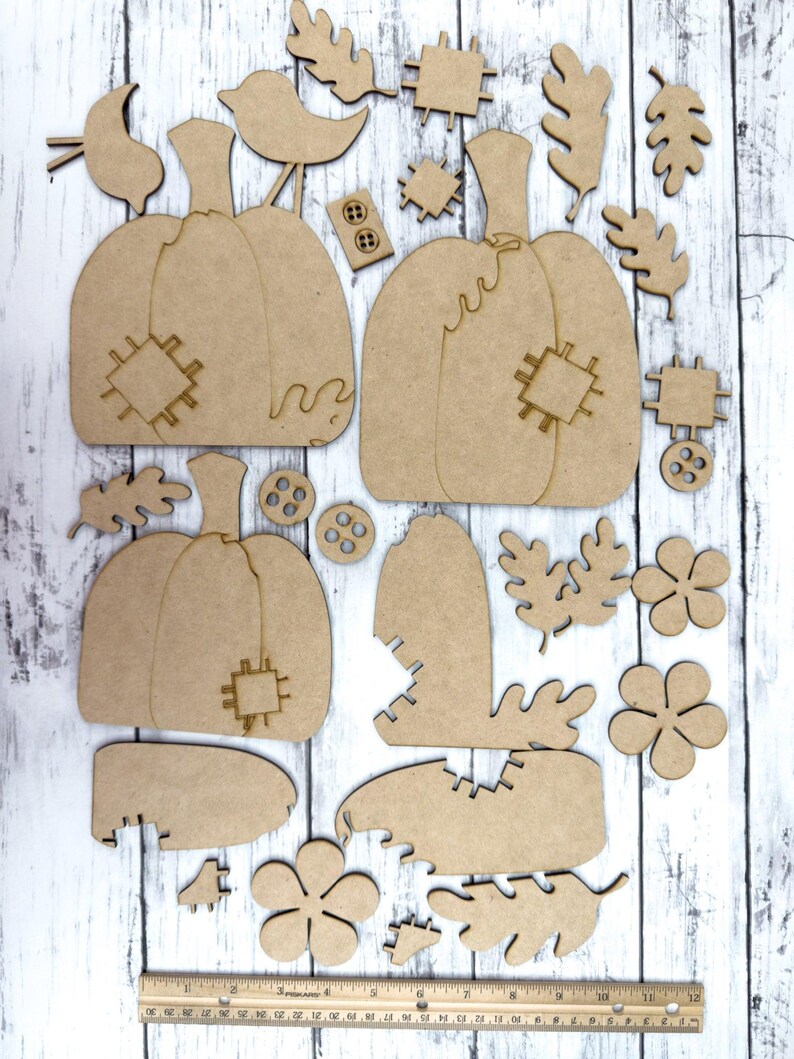 May include: A set of unfinished wooden pumpkin and leaf shapes for crafting. The set includes two large pumpkins, two small pumpkins, a bird, leaves, and flowers. The pumpkins have a stitched design.