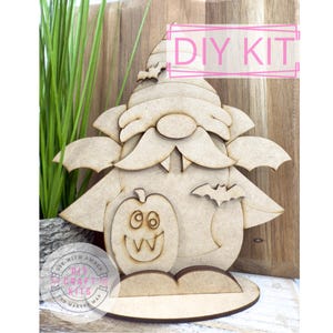 May include: A wooden DIY kit featuring a Halloween gnome design. The gnome has a long beard, a pumpkin on its belly, and bat wings. The kit includes the text "DIY KIT" in a pink rectangle.