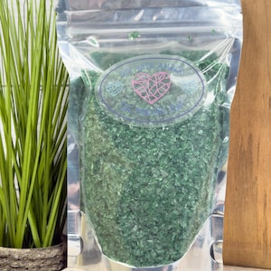 May include: A clear, silver-colored bag filled with small, green, leaf-like pieces. The bag has a label with the text "DIY with Amber" and a pink heart design. A potted plant is visible to the left.