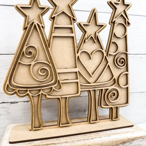 Op de afbeelding: Een set van vier houten kerstboom met sterren op de top. De bomen zijn versierd met swirls, harten en stippen. De bomen staan op een houten basis.