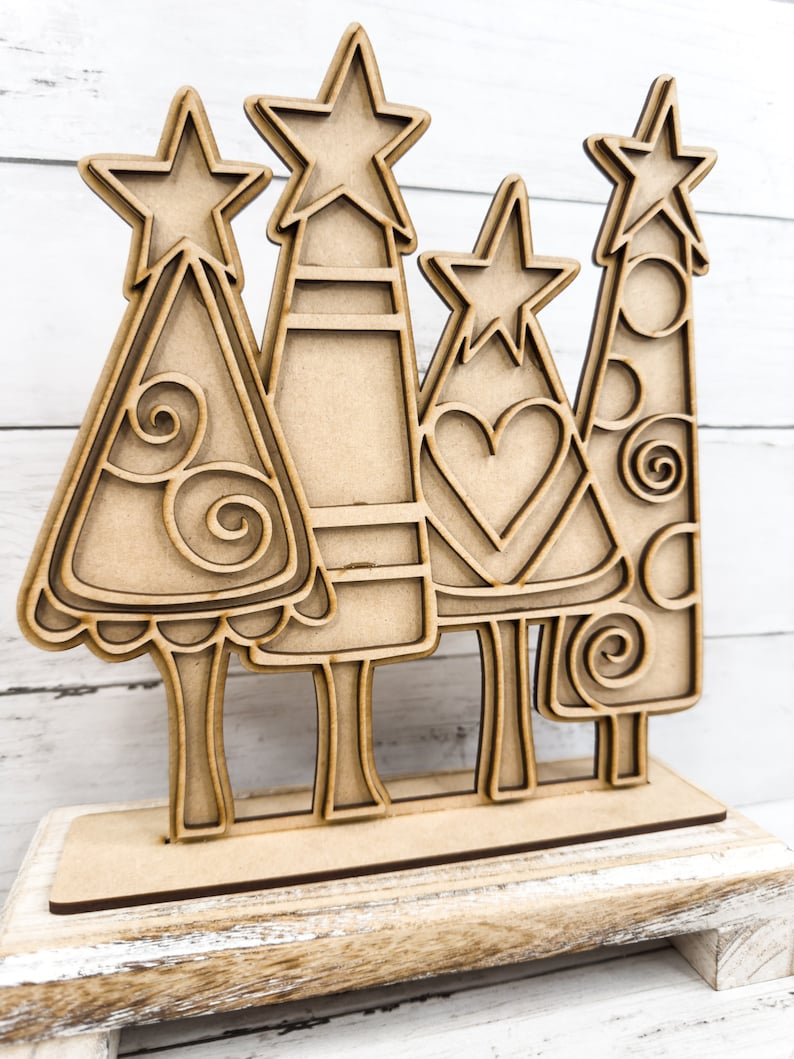 Op de afbeelding: Een set van vier houten kerstboom met sterren op de top. De bomen zijn versierd met swirls, harten en stippen. De bomen staan op een houten basis.