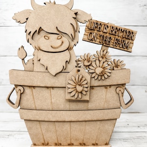 May include: Wooden cutout of a Highland cow in a basket with flowers and a sign that reads "Life is better on the farm".