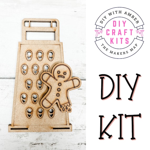 A gingerbread man cookie paired with a tiny grater as a DIY Christmas ornament kit — genuinely crafty, activity-based, and funny in a dark-humor way (grate your cookie man).