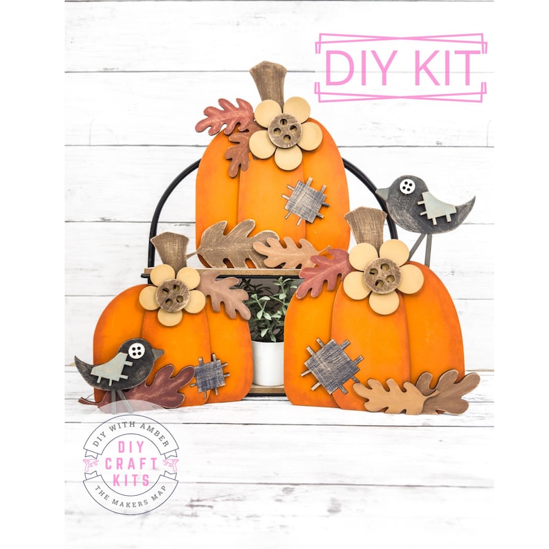 May include: DIY craft kit featuring three orange pumpkins with fall leaves, flowers, and birds. The pumpkins are on a tiered stand. The kit includes all the materials needed to create the project. DIY with Amber The Makers Map.