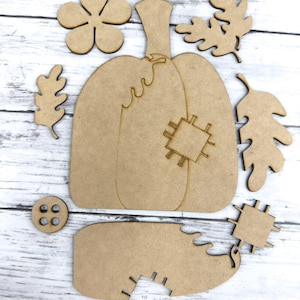May include: A set of wooden craft shapes for a fall-themed pumpkin craft project. The set includes a pumpkin, leaves, a flower, and a button.
