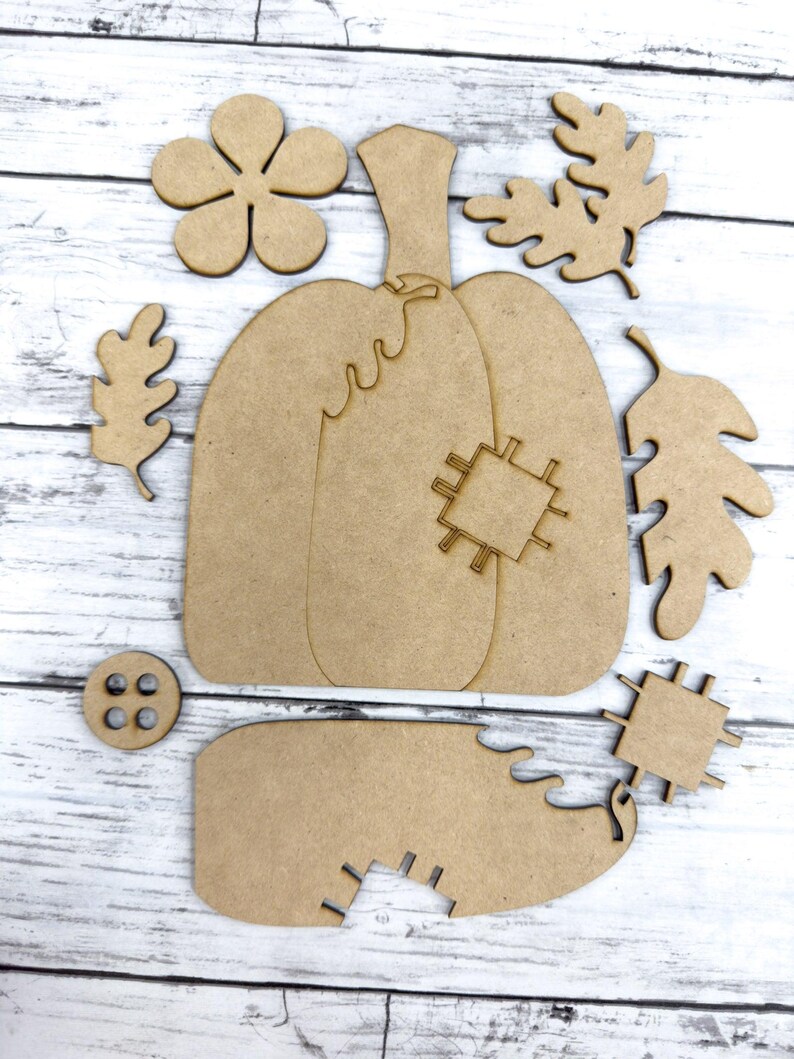 May include: A set of wooden craft shapes for a fall-themed pumpkin craft project. The set includes a pumpkin, leaves, a flower, and a button.