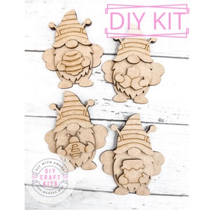 May include: DIY craft kit featuring four unfinished wooden gnome ornaments. Each gnome is holding a honeycomb, a bee, or a jar of honey. The kit is perfect for painting and decorating.