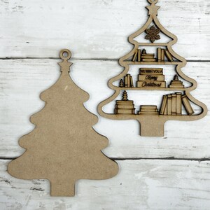 May include: Two wooden Christmas tree ornaments. One is a solid tree shape, the other is a tree with shelves of books and the text "We Wish You a Merry Christmas". Both have a small loop at the top for hanging.