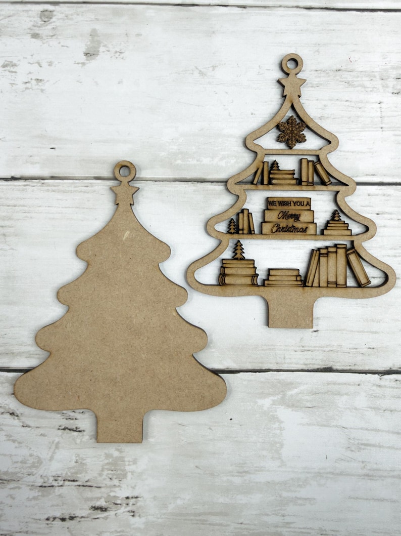 May include: Two wooden Christmas tree ornaments. One is a solid tree shape, the other is a tree with shelves of books and the text "We Wish You a Merry Christmas". Both have a small loop at the top for hanging.