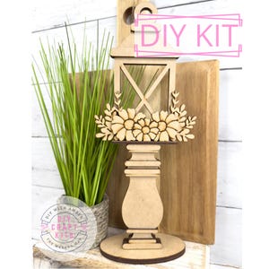May include: DIY craft kit featuring a wooden lantern with floral accents. The lantern is on a pedestal base and has a cutout design. The kit is labeled "DIY Kit".