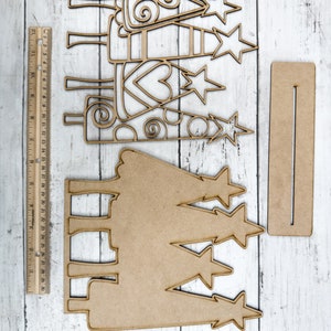 Op de afbeelding: Een set van drie houten kerstboomversieringen met een uitgesneden ontwerp. De bomen zijn versierd met sterren en swirls. De set bevat ook een apart houten bord met een uitgesneden ontwerp.