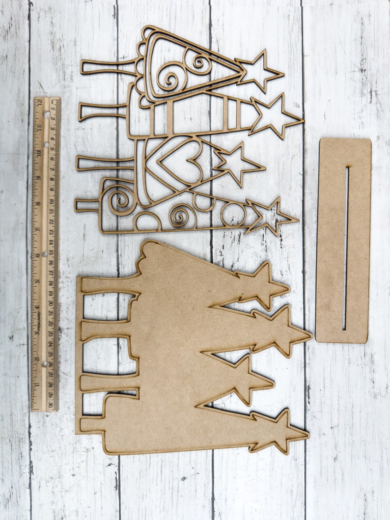 Op de afbeelding: Een set van drie houten kerstboomversieringen met een uitgesneden ontwerp. De bomen zijn versierd met sterren en swirls. De set bevat ook een apart houten bord met een uitgesneden ontwerp.