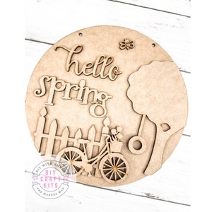 May include: A wooden craft kit featuring a round sign with the words "hello spring" and a bicycle with a basket of flowers. The sign also includes a fence, a tree, and a swing.