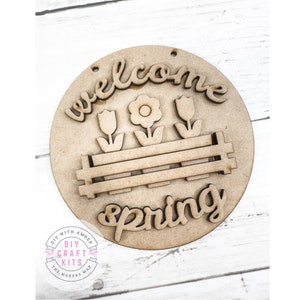 May include: Wooden craft kit featuring a round sign with the words "Welcome Spring" and a design of three tulips in a planter. The sign is unfinished and ready to be painted.