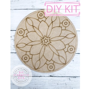 May include: DIY craft kit featuring a wooden mandala design with a star in the center. The mandala is surrounded by a circle of smaller circles. The kit is labeled "DIY Kit" and "DIY with Amber - The Makers Map - DIY Craft Kits".
