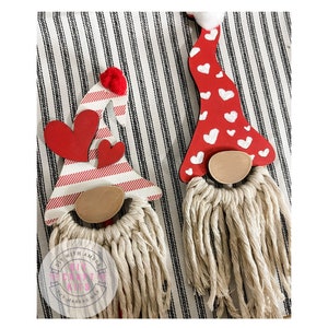 May include: Two Valentine's Day gnomes with red and white striped hats and white yarn beards. One gnome has a red hat with white hearts and the other has a red and white striped hat with two red hearts.