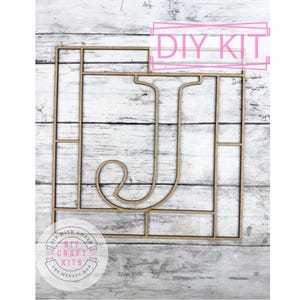May include: A wooden DIY kit featuring the letter "J" within a rectangular frame, divided into smaller sections. The words "DIY KIT" are in a pink rectangle. The kit includes the text "DIY with Amber" and "The Makers Map".