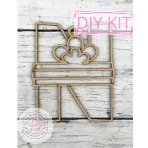 May include: A wooden DIY kit in the shape of a gift box, featuring a decorative bow on top. The words "DIY KIT" are written in pink. The kit is made of light brown wood and is designed for crafting projects.