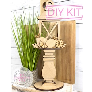 May include: DIY craft kit featuring a wooden lantern with a lemon design. The lantern is on a wooden base and has a window pane design. The kit includes all the pieces needed to assemble the lantern.