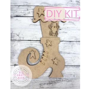 May include: A wooden DIY kit in the shape of a witch's boot, adorned with star and spider cutouts. The boot has a curved toe and lace detailing. The words "DIY KIT" are visible. The kit is designed for crafting.