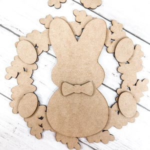 May include: A brown wooden bunny rabbit cutout with a bow tie surrounded by a wreath of brown wooden flowers and eggs.