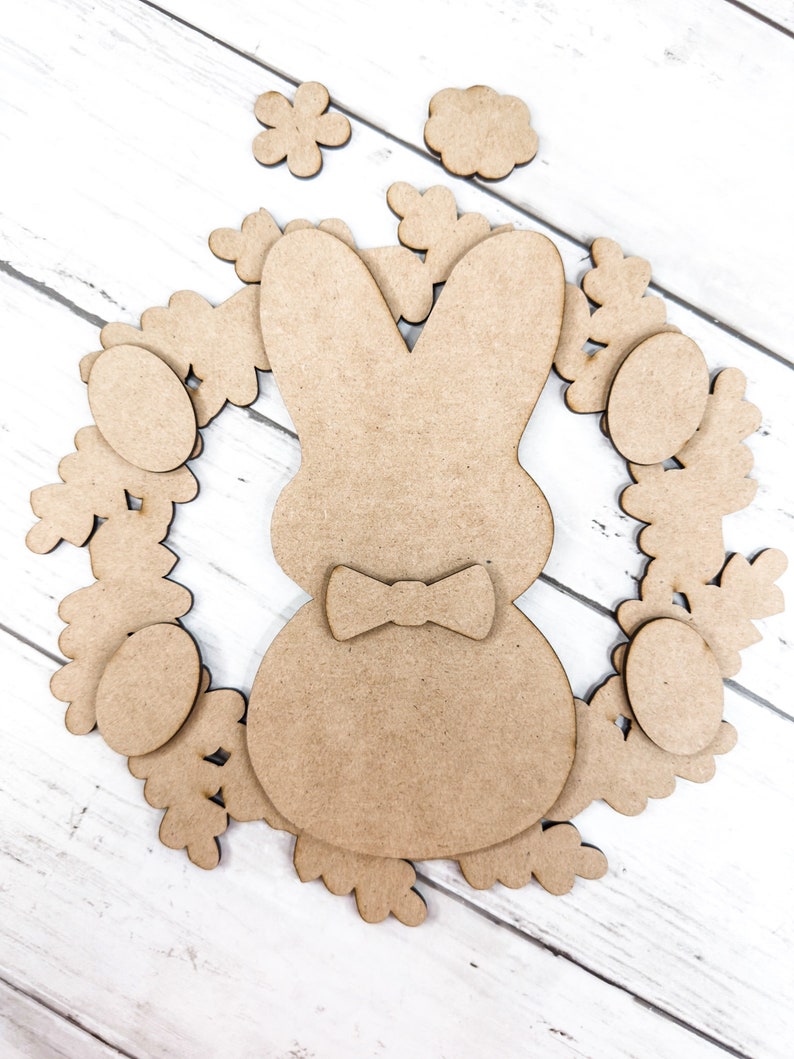 May include: A brown wooden bunny rabbit cutout with a bow tie surrounded by a wreath of brown wooden flowers and eggs.