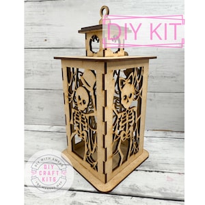 May include: A wooden DIY kit for a Halloween lantern. The lantern features cut-out skeleton designs on the sides and a handle on top. The text "DIY KIT" is visible. The lantern is made of light brown wood.