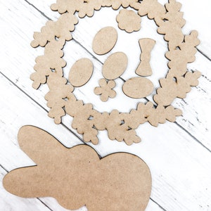May include: A set of wooden craft shapes for Easter, including a bunny, a wreath, eggs, and flowers. The shapes are unpainted and ready to be decorated.