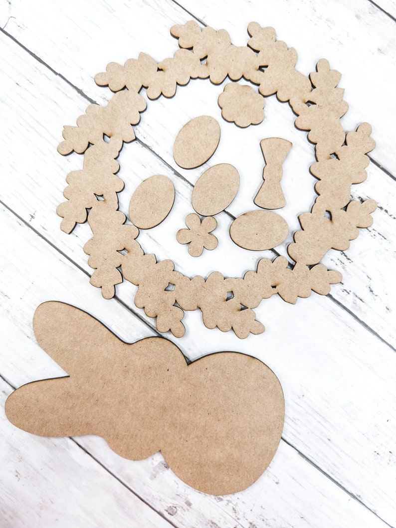 May include: A set of wooden craft shapes for Easter, including a bunny, a wreath, eggs, and flowers. The shapes are unpainted and ready to be decorated.