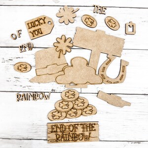 May include: Wooden craft cutouts with a St. Patrick's Day theme. The cutouts include a pot of gold, a horseshoe, a leprechaun hat, a sign that says "End of the Rainbow", a shamrock, and the words "Lucky You", "The", "Of", "End", and "Rainbow".