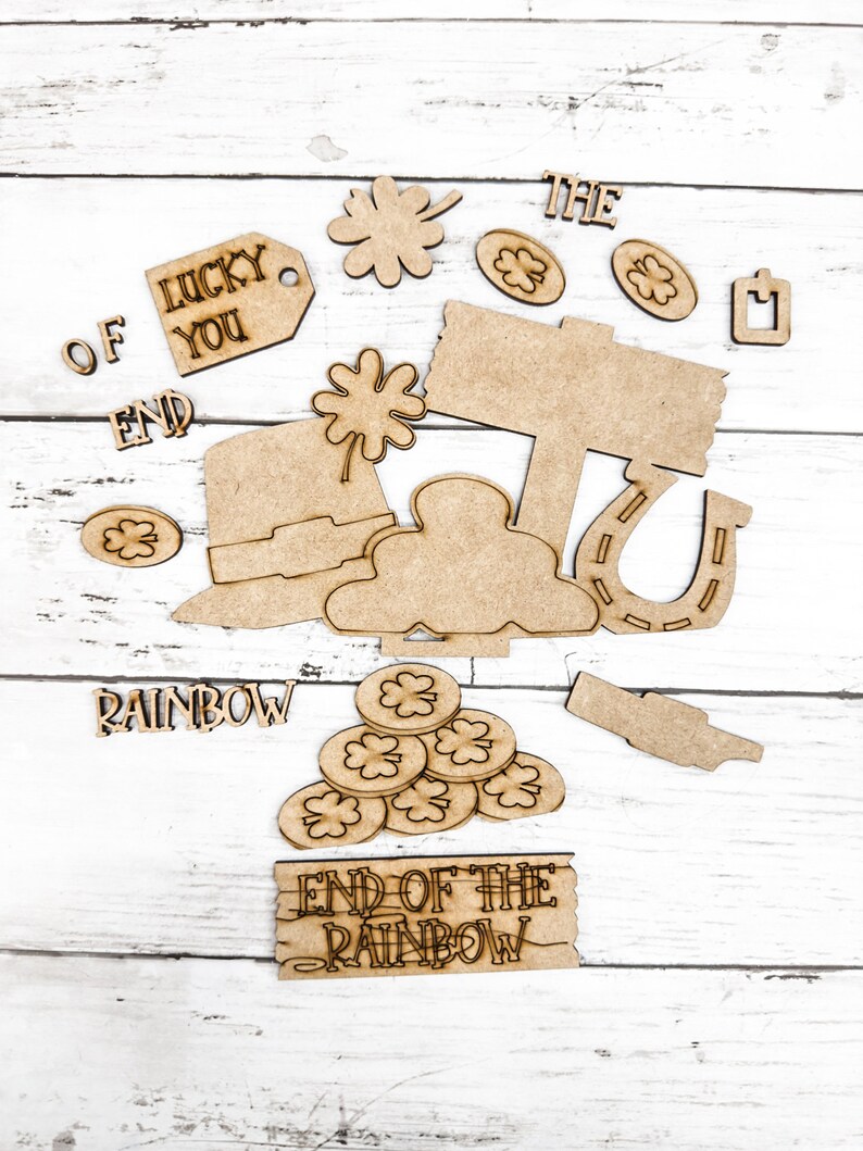 May include: Wooden craft cutouts with a St. Patrick's Day theme. The cutouts include a pot of gold, a horseshoe, a leprechaun hat, a sign that says "End of the Rainbow", a shamrock, and the words "Lucky You", "The", "Of", "End", and "Rainbow".