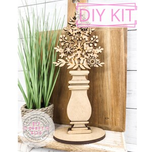May include: DIY craft kit featuring a wooden vase with a floral design. The vase is made of unfinished wood and is ready to be painted or stained. The kit includes all the pieces needed to assemble the vase, as well as instructions. DIY With Amber Craft Kits.