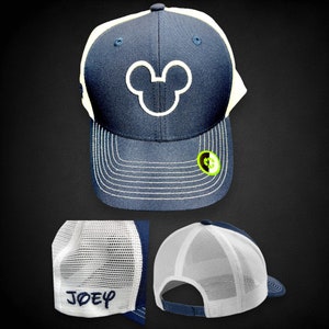 May include: Navy blue and white baseball cap featuring a white outline of Mickey Mouse's head on the front. The cap has a curved brim with white stitching and a white mesh back. The name "JOEY" is embroidered on the back.