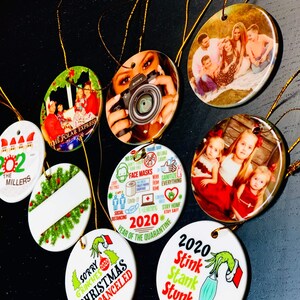 Peut inclure: Un ensemble de dix boules de No&euml;l rondes en c&eacute;ramique blanche avec diff&eacute;rents motifs. Les boules pr&eacute;sentent des images de personnes, du texte et des illustrations. Certains des motifs incluent "The Polar Express", "2020 Ann&eacute;e de la Quarantaine" et "D&eacute;sol&eacute; Grinches No&euml;l 2020 Annul&eacute;".