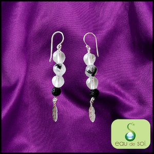 Peut inclure: Boucles d'oreilles en argent avec trois perles transparentes avec des inclusions noires et une perle de lave noire et un charme en plume d'argent.