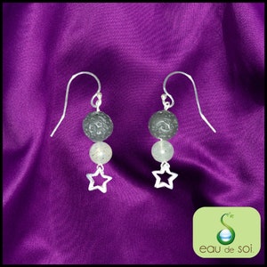 Peut inclure: Boucles d'oreilles pendantes en argent avec des perles de lave noire et de pierre de lune blanche, et un charme d'étoile en argent. Les boucles d'oreilles sont sur un fond violet.