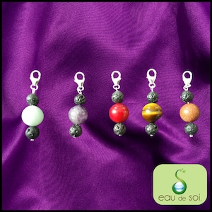 Peut inclure: Cinq pendentifs de charme argentés avec des perles de lave noire et une variété de perles de pierres précieuses colorées. Les pierres précieuses sont vertes, violettes, rouges, brunes et orange. Les breloques sont attachées à un clip argenté.