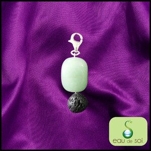 Peut inclure: Un charme en argent avec une pierre de jade vert clair et une pierre de lave noire. Le charme est suspendu sur un fond violet.